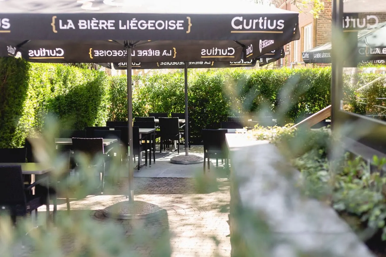 La terrasse le long de la haie, tables dressées sous les parasols